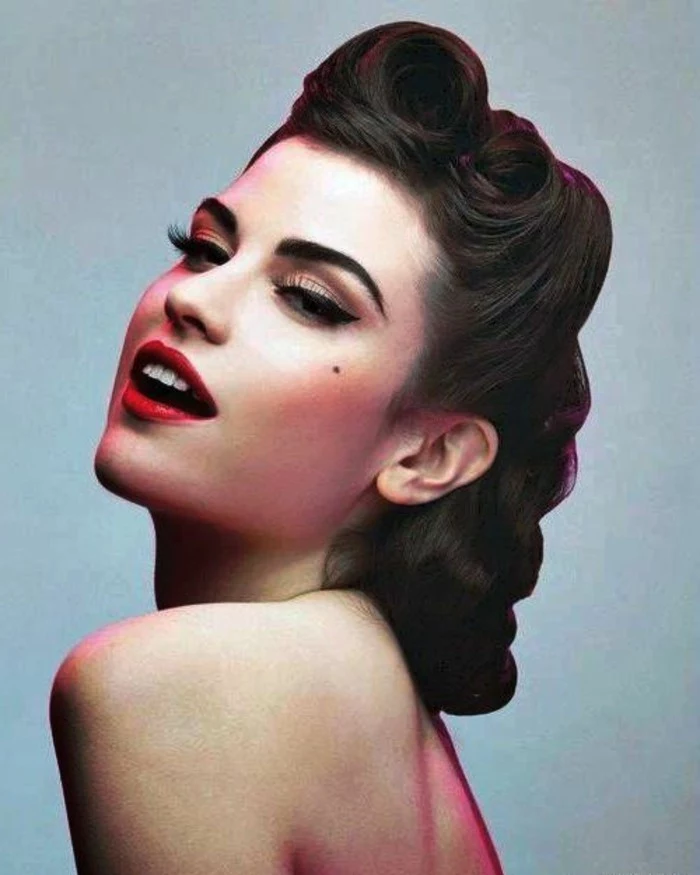 close up of woman with brown 1940's pinup hair, victory rolls and curls, red lipstick white teeth, eyeliner and fake lashes, mascara and a beauty spot, bare shoulders