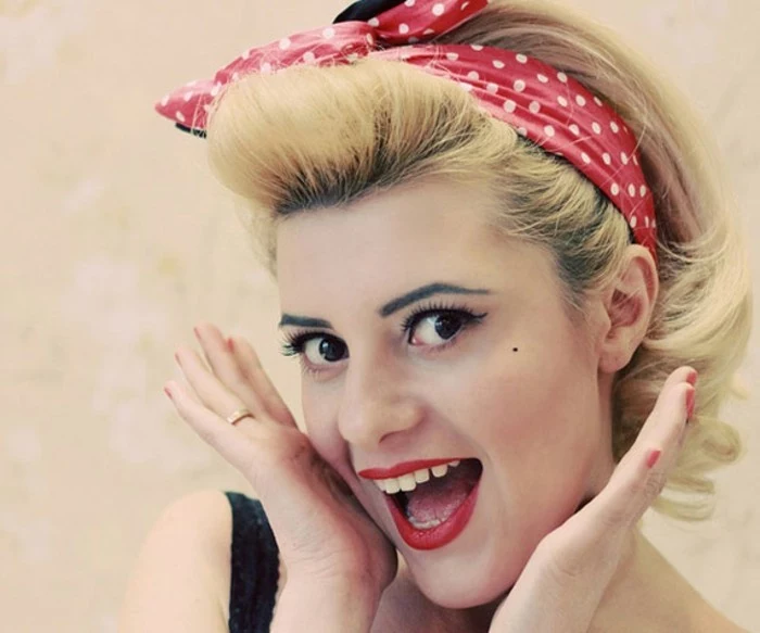 close up of happy smiling woman, open month white teeth and red lipstick, black eyes fake lashes eyeliner and mascara, dyed blonde hair red bandanna with white polka dots