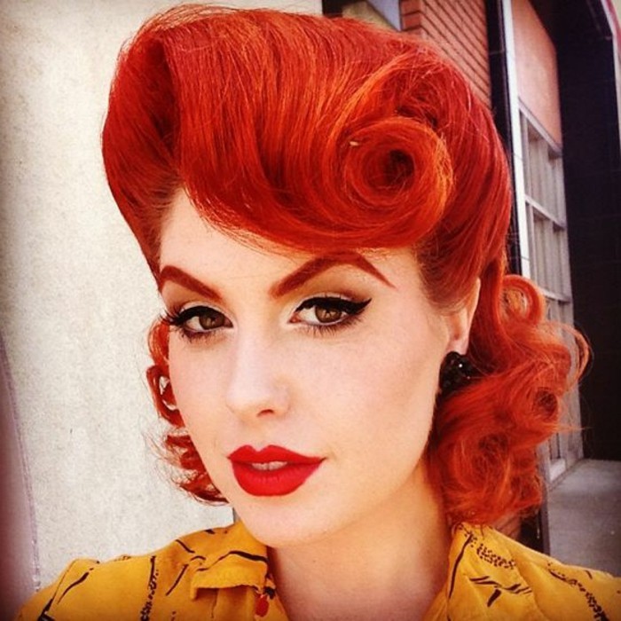 close up of woman with bright red hair, curled in retro style, bright red lipstick and heavy eye make up, big arched eyebrows and a yellow top