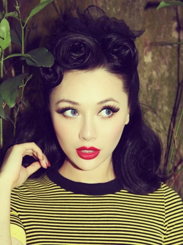 rockabilly hair, pale girl with dark hair done in retro victory rolls, with red lipstick and nail polish, big fake eyelashes with mascara and eye liner, yellow top with black stripes