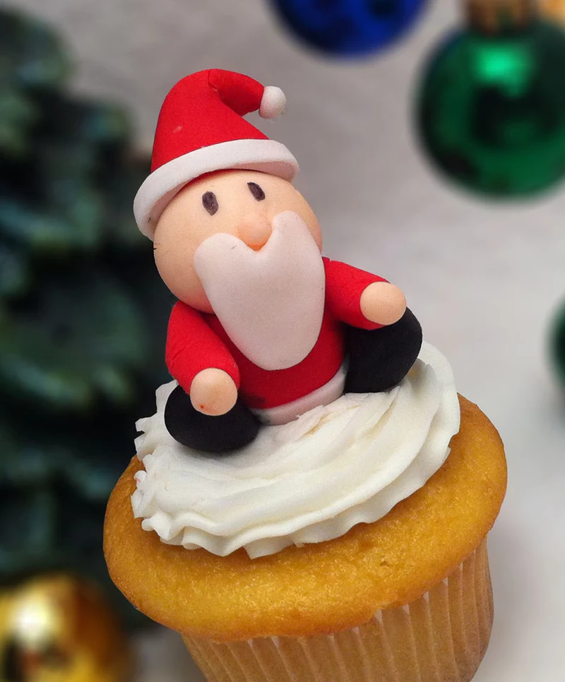 close up of small plain cupcake with white icing, decorated with small and simple red, black orange and white santa fondant shape