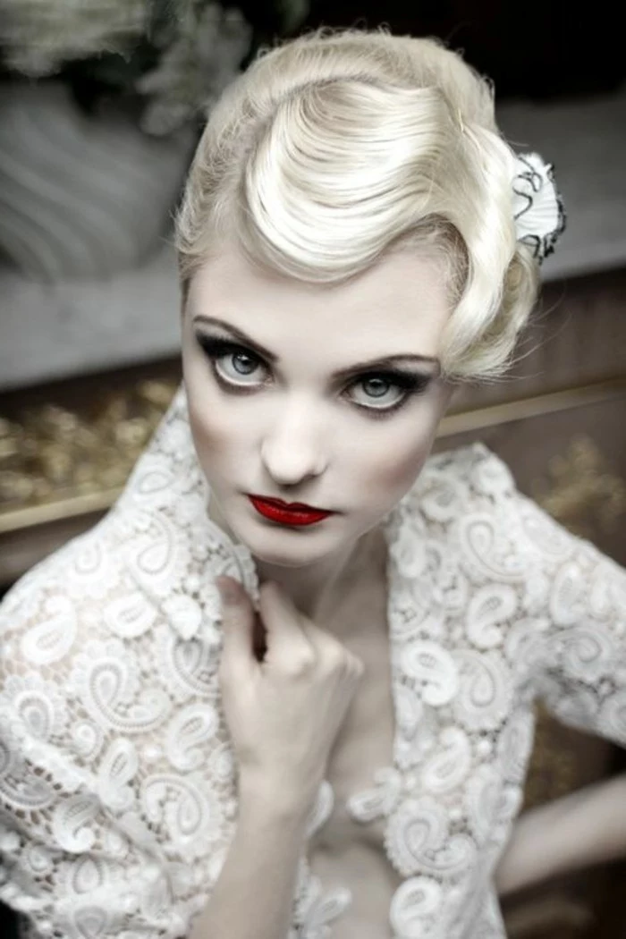 pin up girl hairstyles, retro 1920's short wavy hairstyle, worn by pale platinum blonde woman, with heavy eye make up red blush and lipstick, white paisley lace top
