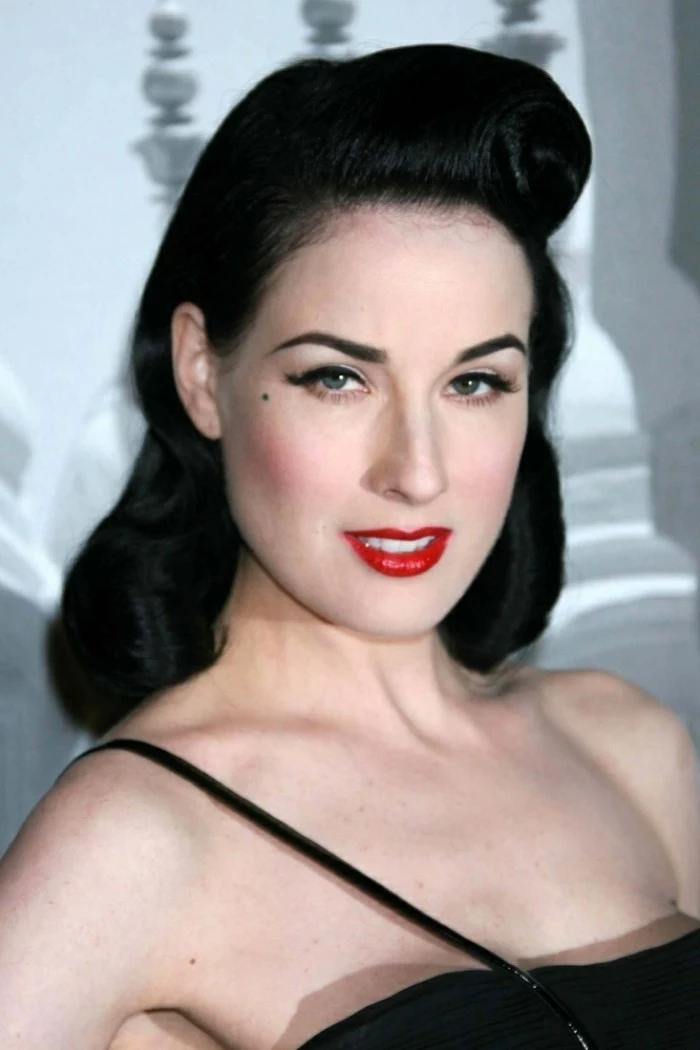pinned up hairstyles for long hair, dita von teese, black long hair with rolled back bangs, red lipstick blush eyeliner fake lashes and mascara, black top with one strap