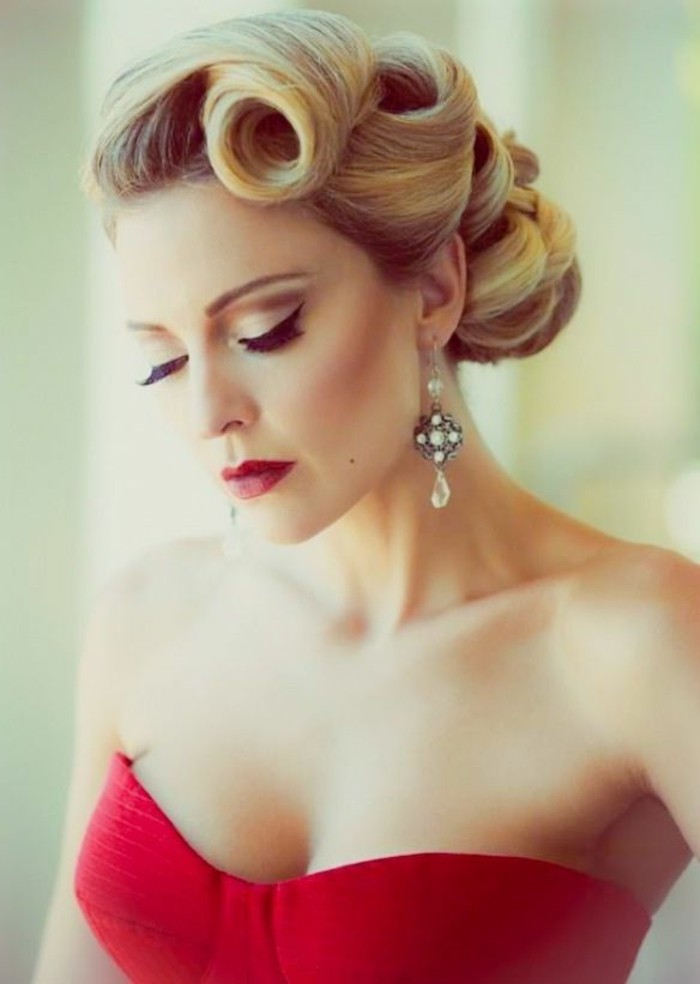 serious-looking woman with blonde hair with retro victory curls, pearl earrings and a red strapless top, red lipstick fake eyelashes and eyeliner 