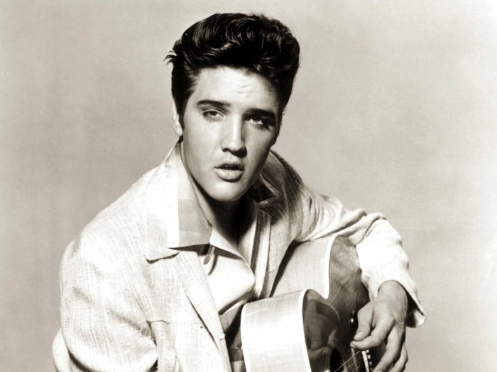 vintage black and white photo of elvis presley, light blazer and shirt with big collar, gelled up wavy hair, holding acoustic guitar with fingers on strings