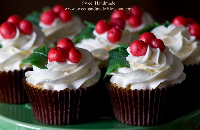 a batch of cupcakes in brown wrappers, with white icing decorated with cranberry berries and leaves, on green dish