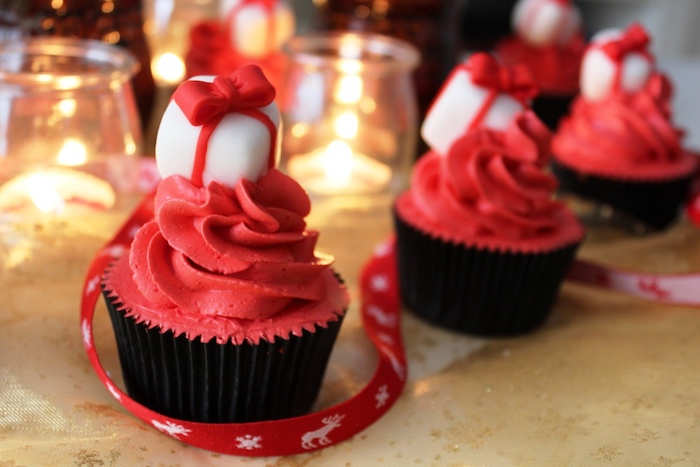 holiday cupcakes, a few cupcakes with black wrappers and red creamy icing, decorated with white and red fondant present shapes, candles and festive red ribbon