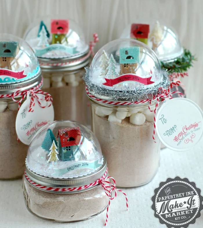 diy gift ideas, several jars of different sizes, filled with cocoa and marshmallows, with snow globes on their lids featuring little house figurines and colorful strips of paper