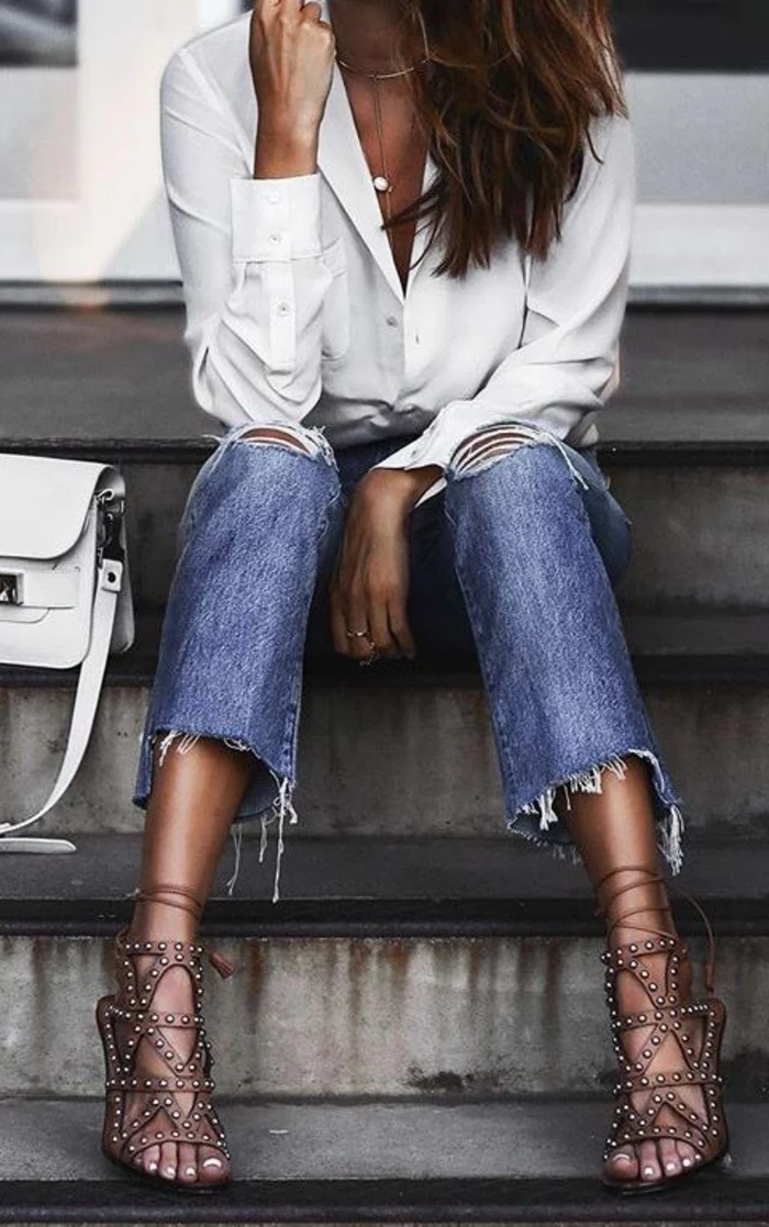 close up of female torso, sitting on steps and wearing cut-off ankle jeans, white formal shirt and strappy brown sandals with studs