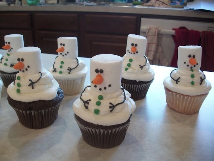a batch of chocolate and vanilla cupcakes, decorated with marshmallow creme and actual marshmallows, made to look like snowmen with icing and fondant