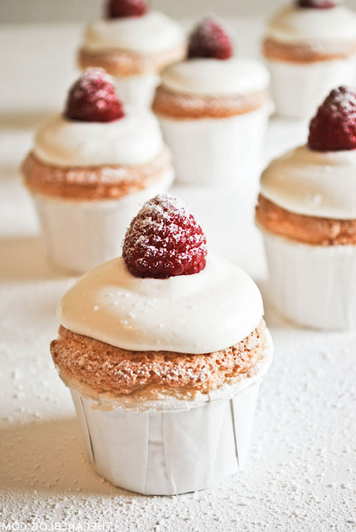 holiday cupcakes, six cupcakes in white wrappers, with white frosting, decorated with raspberries and dusted with powdered sugar