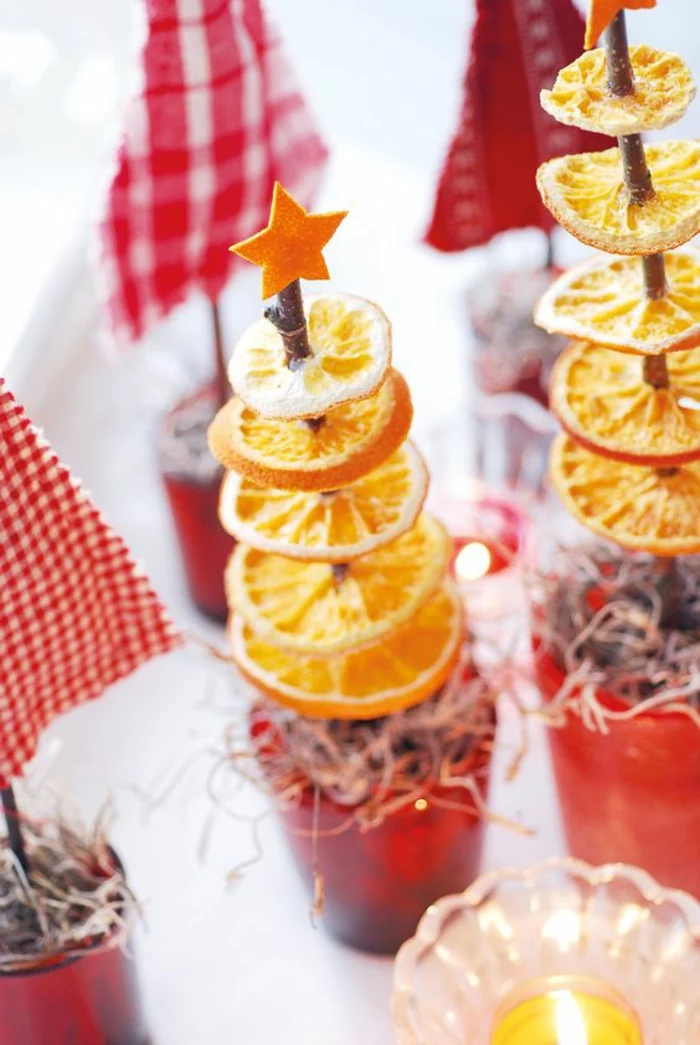 diy christmas gifts, two christmas tree ornaments, made from dried orange slices spiked on a twig, with little orange cut out star on top, near other decorations, small candle