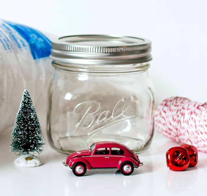 diy gift ideas, two small red bells, Christmas tree figurine and a red toy car, empty clear jar with screw lid, bag of fake snow and red and some white string