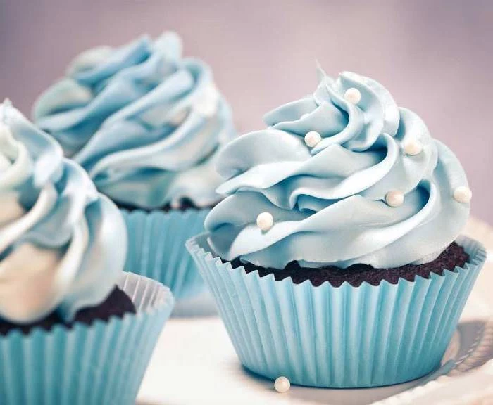 christmas baking ideas, three chocolate cupcakes in light blue wrappers, with light blue creamy frosting, decorated with white pearls