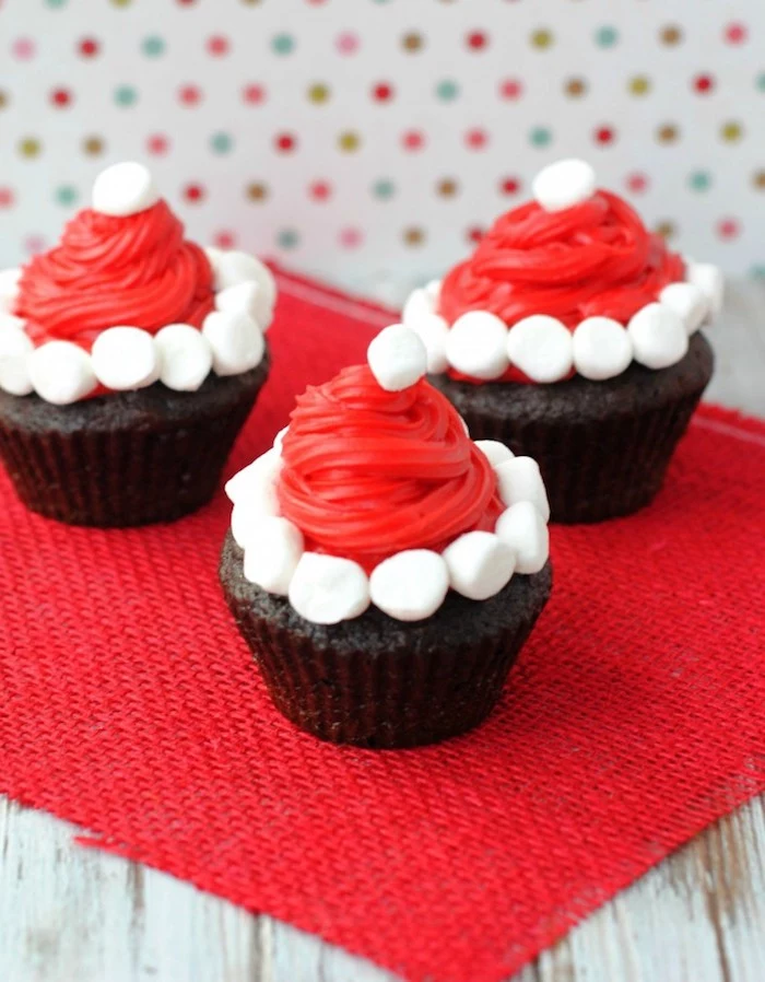 chocolate cupcakes images, three chocolate cupcakes, decorated with santa hats, made from red icing and small white marshmallows