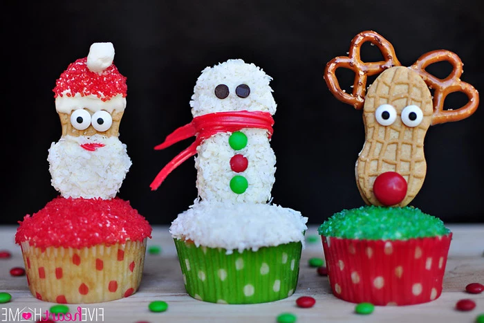 three cupcakes with red, white and green sparkling sugary frosting, decorated with cookies made to look like santa, snowman and rudolph