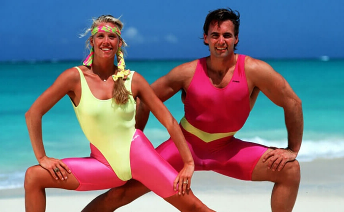 80's fashion for men, woman and men working out on beach, wearing neon colored yellow and pink bodysuits, pink cropped sport leggings and colorful headband, azure blue sea and sky in background
