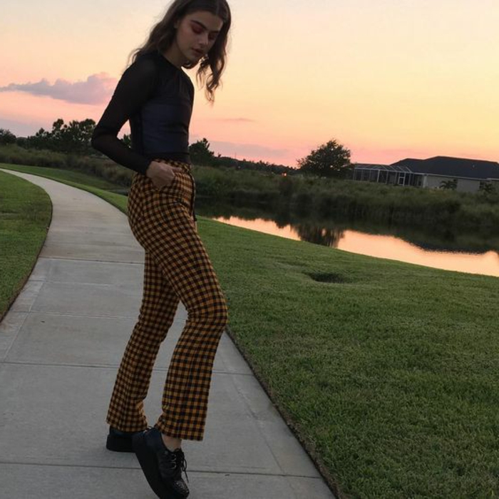 throwback thursday outfits, young slender girl with mid-length wavy brown hair, black top and yellow checked trousers, hands in pockets and black platform shoes