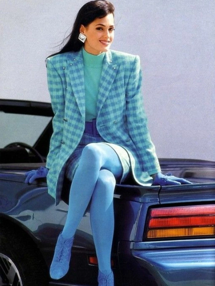 80s fashion, young smiling brunette with big square earrings, sitting on a blue retro convertible car, wearing a checked blue skirt suit with oversize blazer, opaque blue tights blue shoes and blue gloves