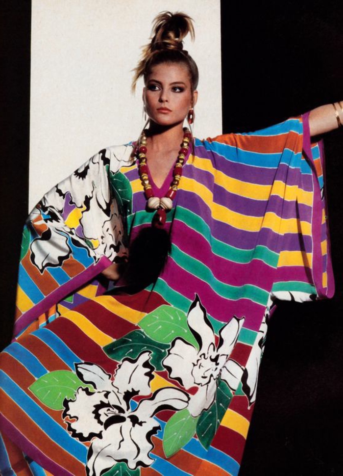 throwback thursday outfits, woman with blond top ponytail, wearing a wide-fitting dress with differently colored stripes and flower motives, over-sized ethno necklace, black and white background