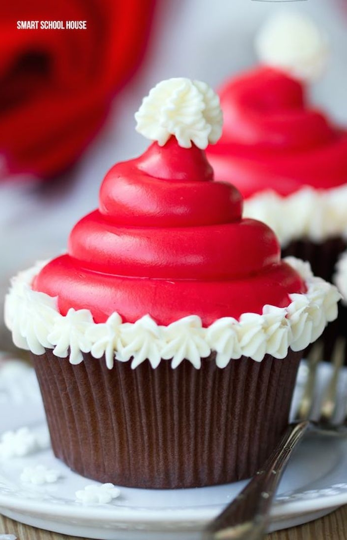 cupcake with dark wrapper, decorated with small santa hat made from smooth red icing and white cream frosting 