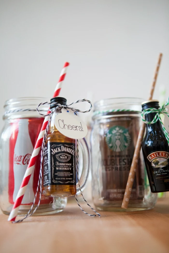 christmas crafts for adults, a can of coke in a clear jar with handle, a small bottle of whiskey and red and white straw tied to jar, a can of coke in clear jar with handle, brown spotted straw and small bottle of liqueur tied with green and white string 