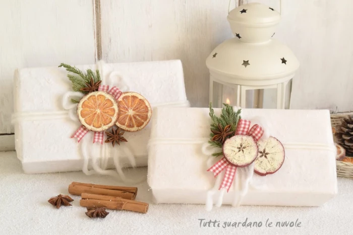 christmas crafts for adults, two gifts wrapped in fluffy white paper, tied with soft chunky white tread, decorated with painted wooden circles, green twigs and star anise, near cinnamon sticks and a white tin lantern