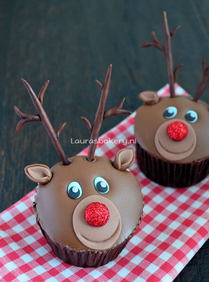 two cupcakes with smooth chocolate icing, made to look like reindeer, with fondant antlers and ears, and red sparkly noses, on red and white checkered cloth