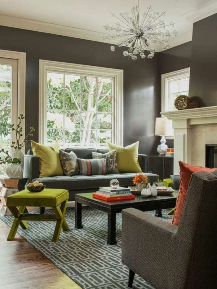two tone living room walls, dark brown walls with plaster details, white ceiling and glass chandelier, grey and white carpet, dark bluish-grey sofa with lime green and colorful cushions, lime green chair and wooden table