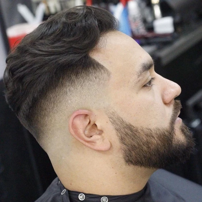 undercut fade, man in profile with hair long on top and shorter on the sides, with beard and mustache, wearing a black hairdresser's robe