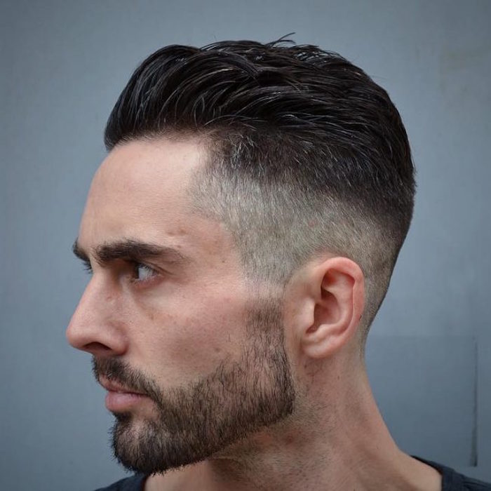 undercut fade, close up of man with black and grey hair, with mustache and beard, facing sideways and looking serious, with hair clipped short on sides and swept back on top