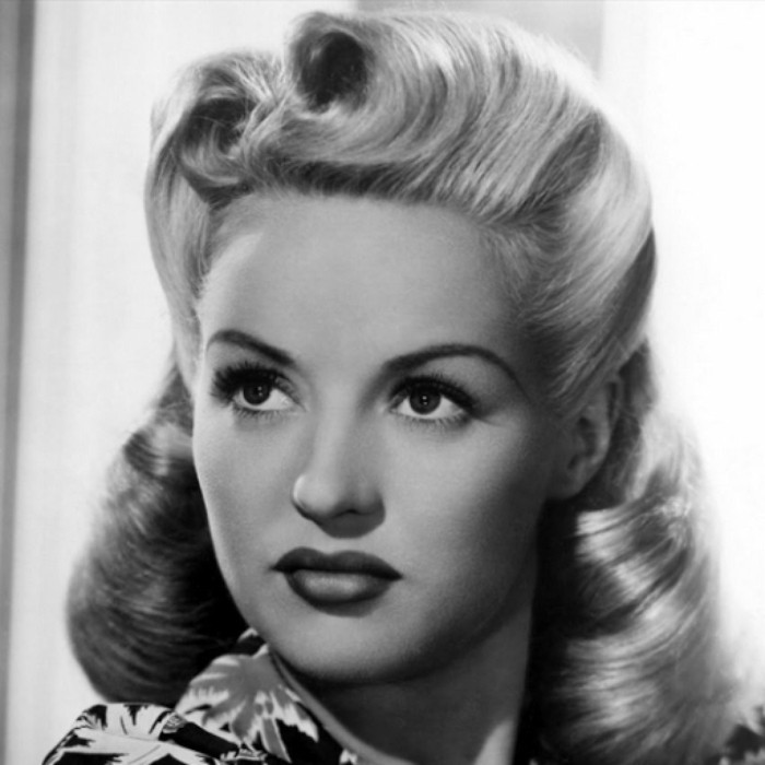 pinup hair, vintage black and white photo of woman with light hair and victory rolls, dark lipstick and big fake eyelashes, palm-tree printed top