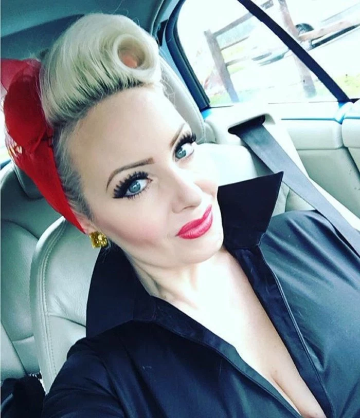 close up of woman in car with heavy make up, fake lashes mascara and vibrant lipstick, dyed blonde hair with victory roll, red bandanna and black top