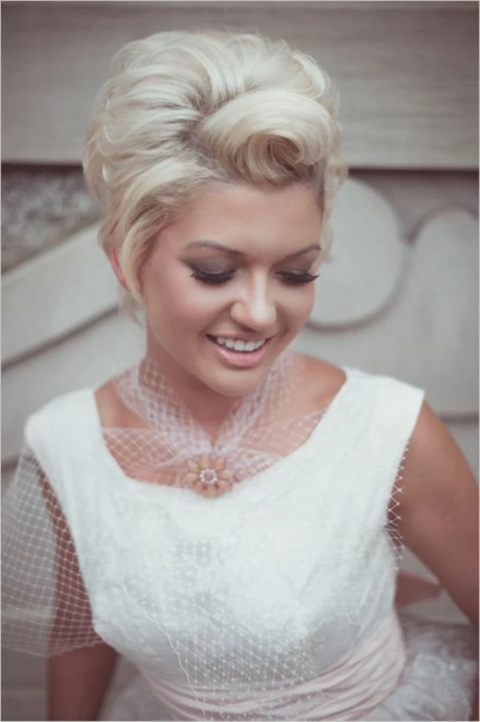 happy smiling woman with short platinum hair, styled with victory rolls, dark smoky eye make up, pale nude lipstick, white dress with white mesh details and flower broach 