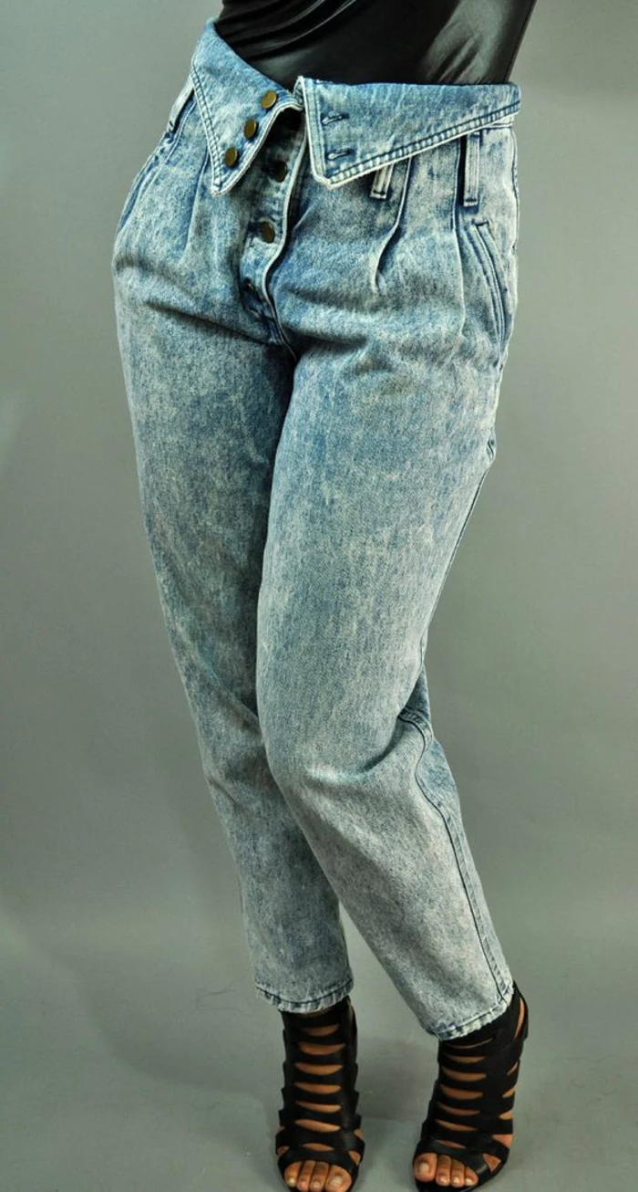 close up of woman's lower half, wearing high-wasted acid wash jeans with button fold over detail, black sandals with many straps and black shiny top