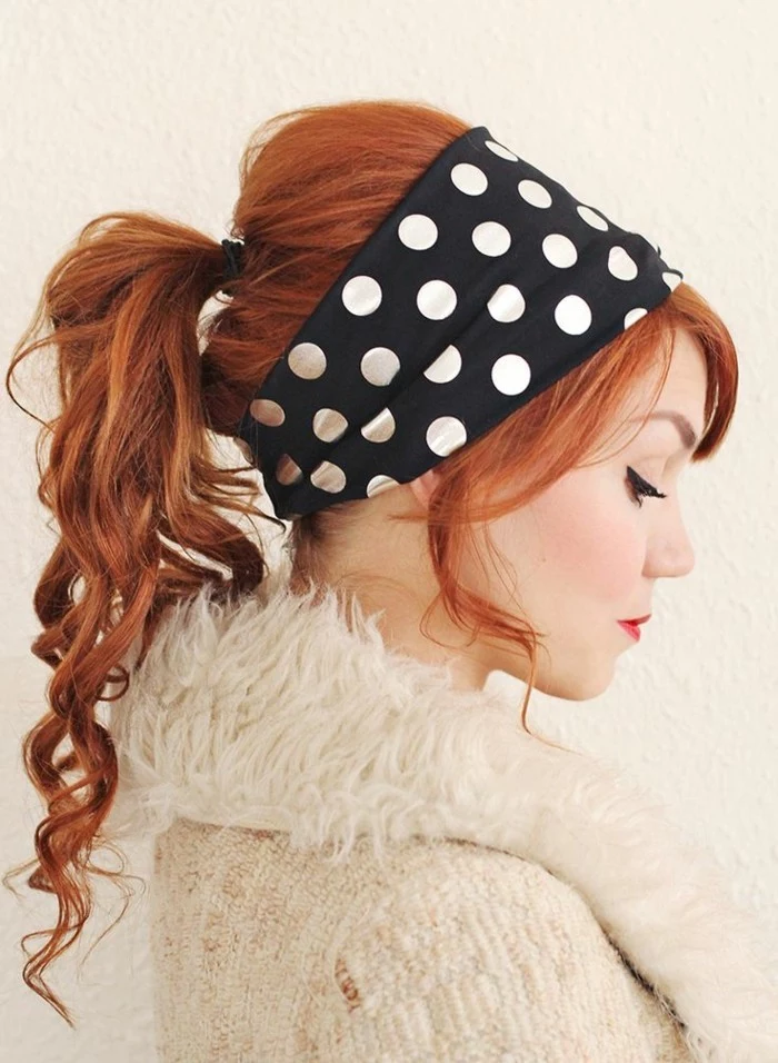 pin up hairstyles, copper red or ginger haired woman, hair tied in curly ponytail, eyeliner and red lipstick, wearing a fluffy cardigan and looking down