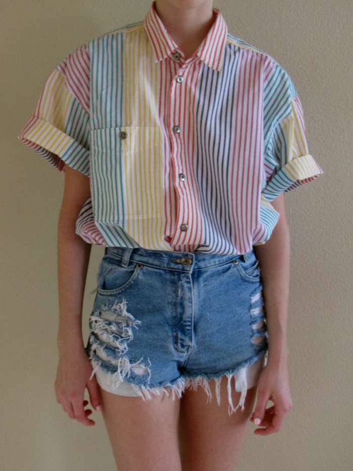 woman wearing over-sized shirt with cropped rolled sleeves and differently colored stripes, paired with ripped and distressed denim shorts