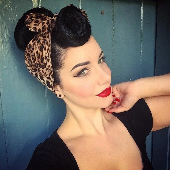 rockabilly hair, smiling woman with black hair, victory roll curled bangs and an animal print bandanna, heavy makeup featuring very bold eyeliner and bright red lipstick