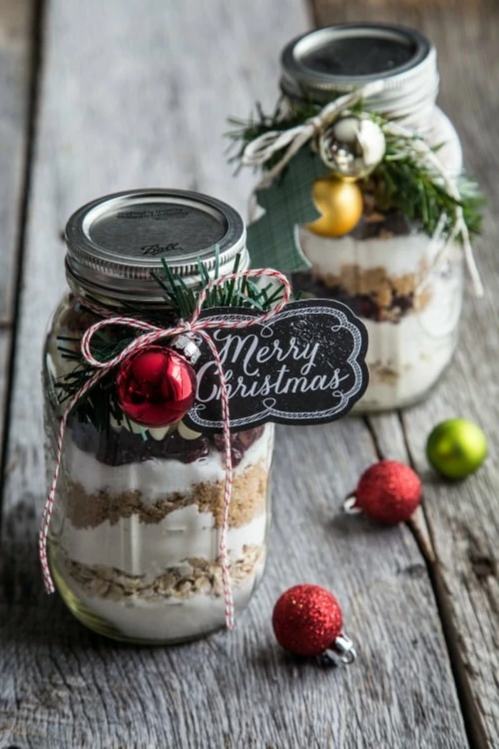 family christmas gifts, two jars containing layers of sugar flour and nuts, decorated with pine twig and xmas tree ornaments, black label tied with red and white string, red green yellow and silver ornaments 