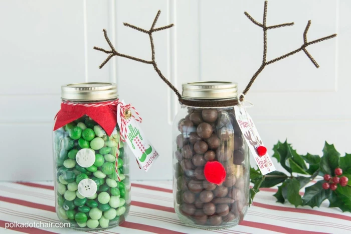 family christmas gifts, clear mason jar with screw-top lid, with 2 green buttons and a red collar containing green candy, jar with red pom-pom nose and wire antlers containing chocolate candy, a branch of holly