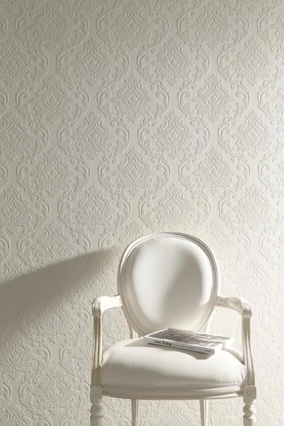 ornamental wallpaper in light cream, featuring Victorian-style symmetrical floral pattern, ornate white chair with magazine