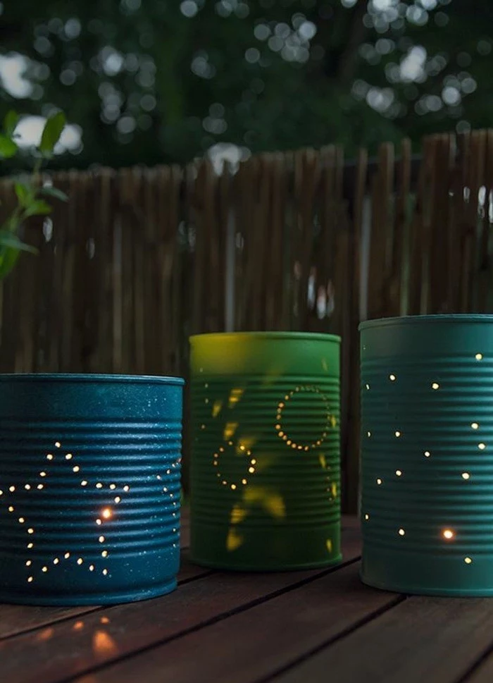 three luminaries made from cans in blue and green, with little holes forming different shapes, lit from within