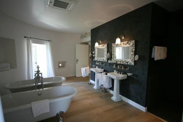 bathroom makeovers, light wooden floor, one wall decorated with dark wallpaper and two ornate mirrors, other walls painted white, two white ceramic tubs and sinks