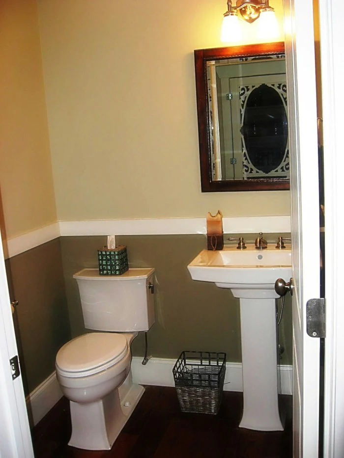 bathroom remodel, pale yellow and dark khaki walls with white detail, dark wooden floor, white ceramic toilet and sink, mirror in wooden frame