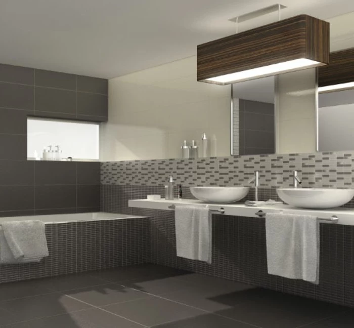 dark grey floor tiles, large wall mirror, two white sinks, inbuilt bath with dark grey mosaic, more mosaic tiles on wall, in different shades of grey
