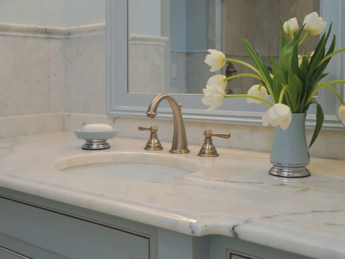 bathroom designs, close up of pale blue sink with marble top surface, yellow metallic taps, mirror and a vase with tulips