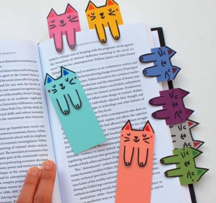 best friend gift ideas, hand holding open book, decorated with eight bookmarks in different colors, shaped like cats