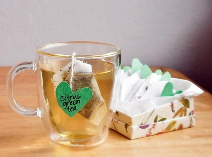 what to get your best friend for her birthday, clear glass mug, containing tea and a teabag, with handmade heart-shaped green label, more teabags in a box nearby