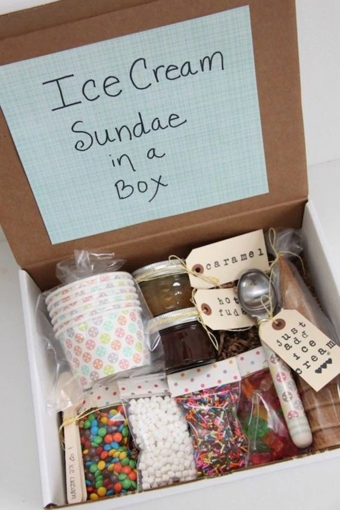 open cardboard box, containing plastic bags with ice cream cones, spoons and paper bowls, many different types of ice-cream toppings