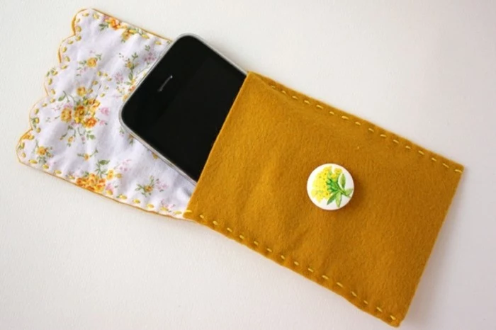 best friend christmas gifts, black smartphone inside a hand-stitched pocket, made from felt in mustard color, with white and yellow lining, and a flower pin decoration